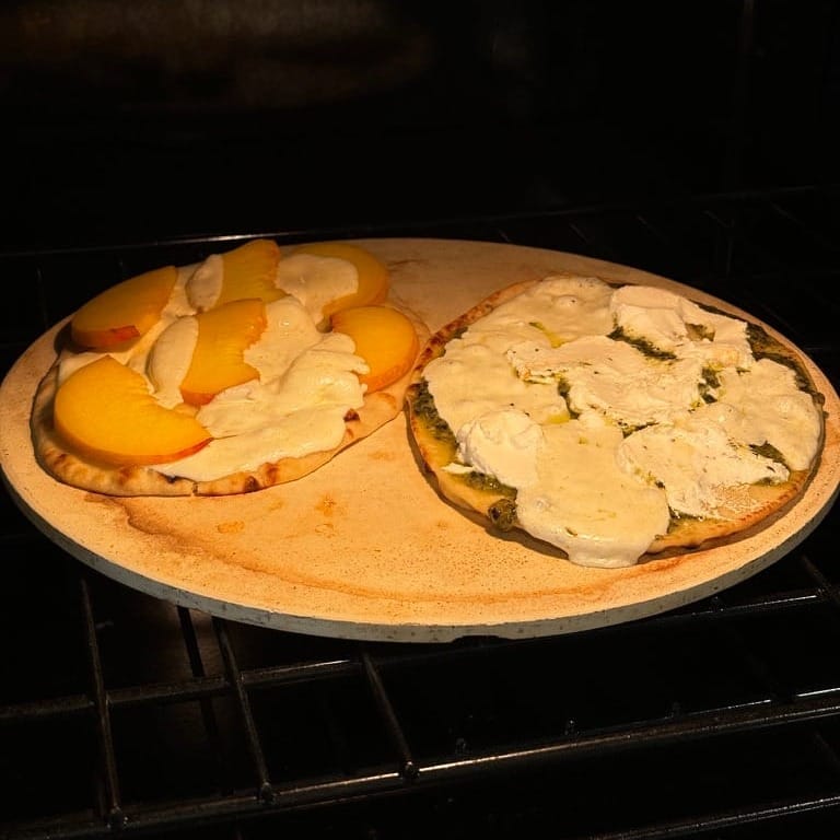 Two flatbreads on naan in my oven: mozz and peaches on the left (we topped with a balsamic reduction and basil), homemade purple pesto, mozz, and ricotta on the right.