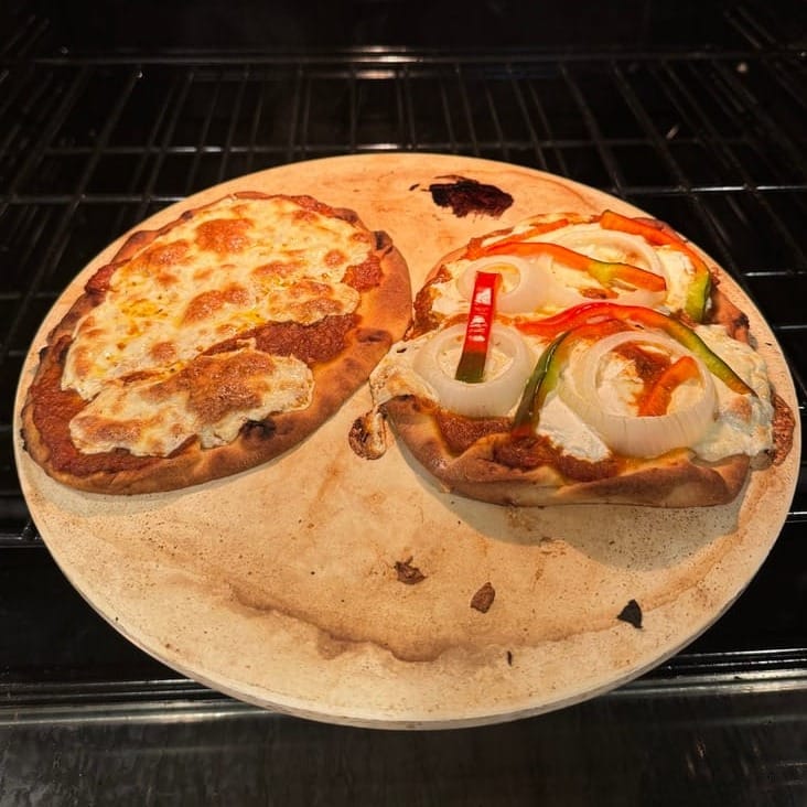 Two flatbreads on naan in my oven: sauce with mozzarella on the left, sauce with mozzarella and peppers and onions on the right.