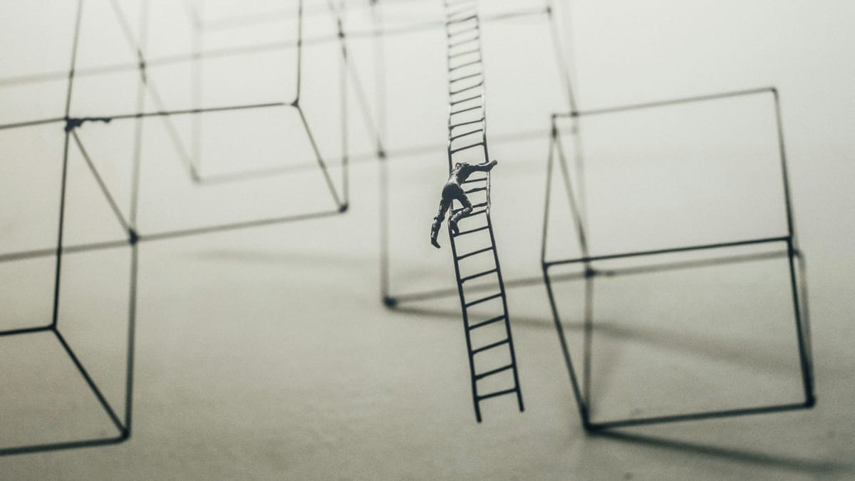 A small man descending a small metal ladder that just ends in midair. Other geometric metal sculptures hang nearby.