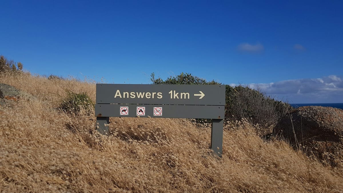 Long grasses, a bush, a body of water on the horizon, and a sign that says "Answers: 1 kilometer".